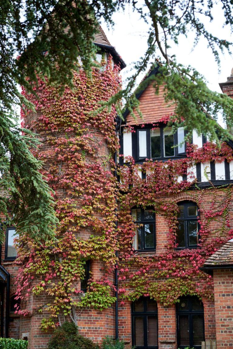 Tower and front of Careys Manor Hotel in autumn with red leaves on brickwork