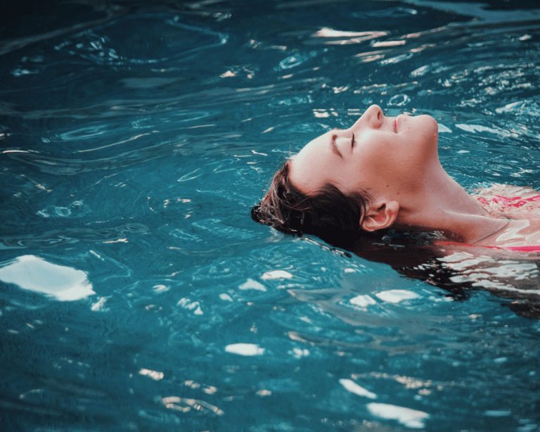 Close up shot of woman floating in pool with eyes closed looking relaxed and happy