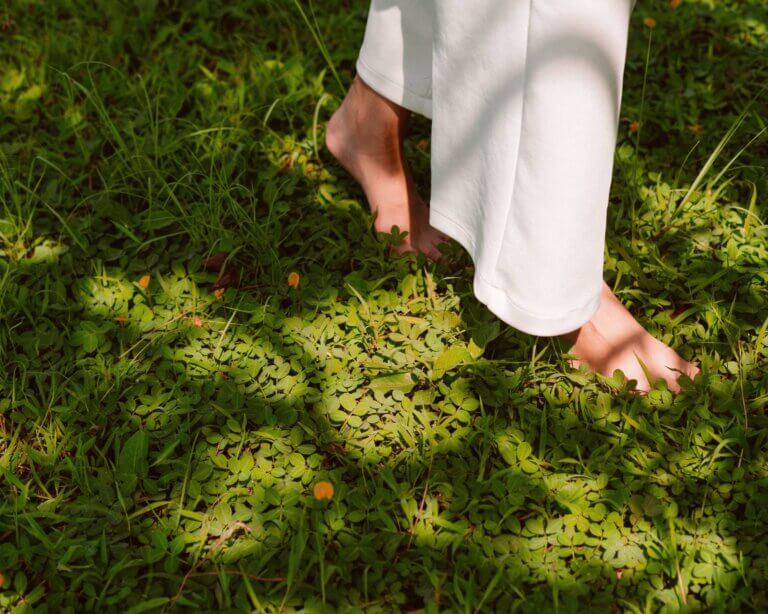 Woman in white trousers walks barefoot on green grass in sunny weather