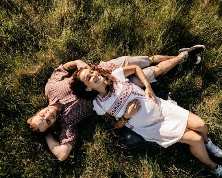 Pregnant couple lie in a field on grass - Babymoon break in the New Forest