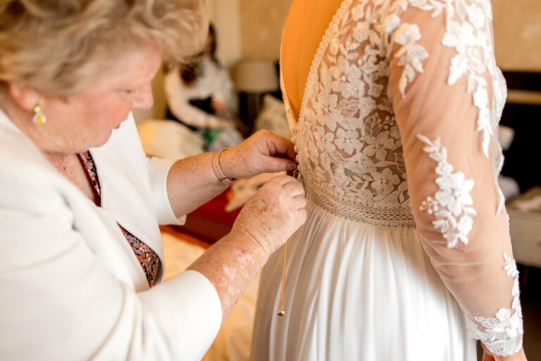 Mother of the bride fastens the brides dress at the back