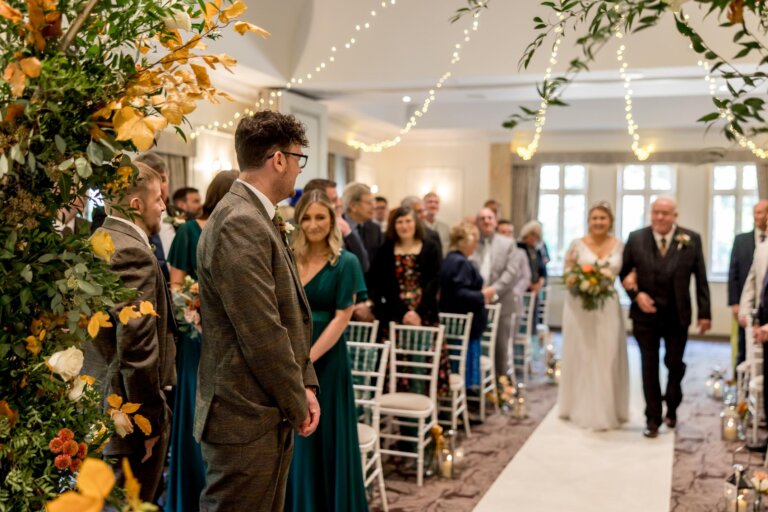 Bride walks down the aisle towards the camera where the groom waits.