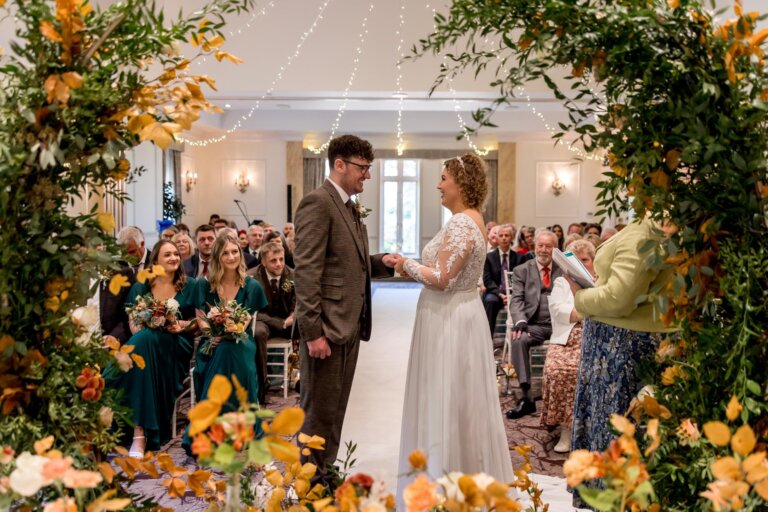 Bride and groom stand facing each other framed by the floral moon arch