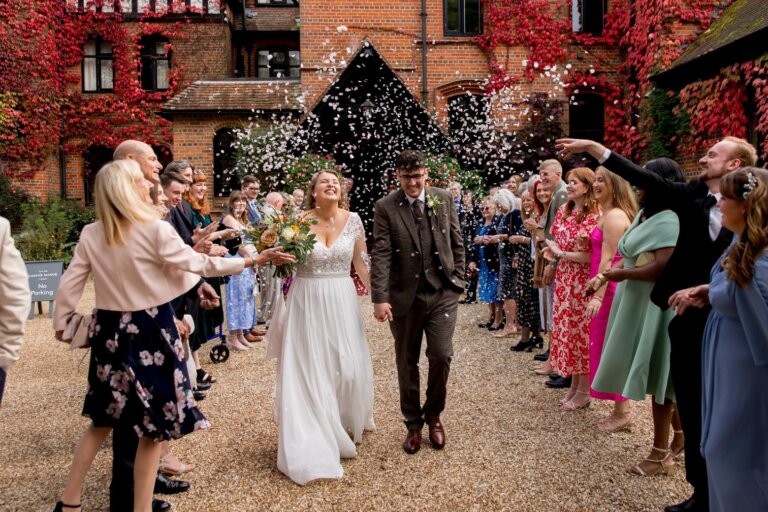 Bride and Groom walk away from the entrance of Careys Manor while guests throw confetti from either side