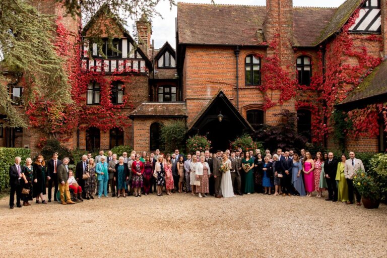 Whole wedding party gather for a photo in front of Careys Manor which is covered in the red, autumnal ivy